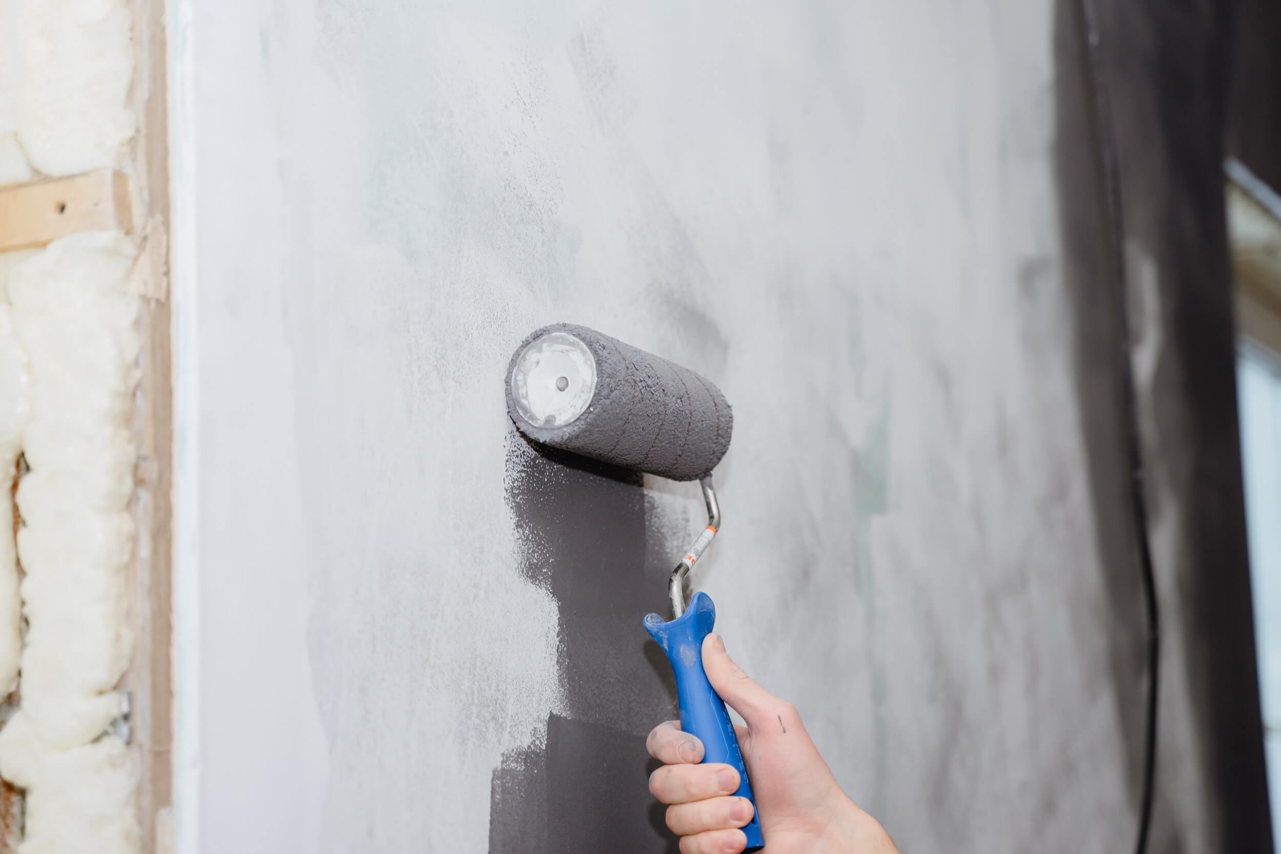 A person uses a paint roller to paint a wall with dark paint.